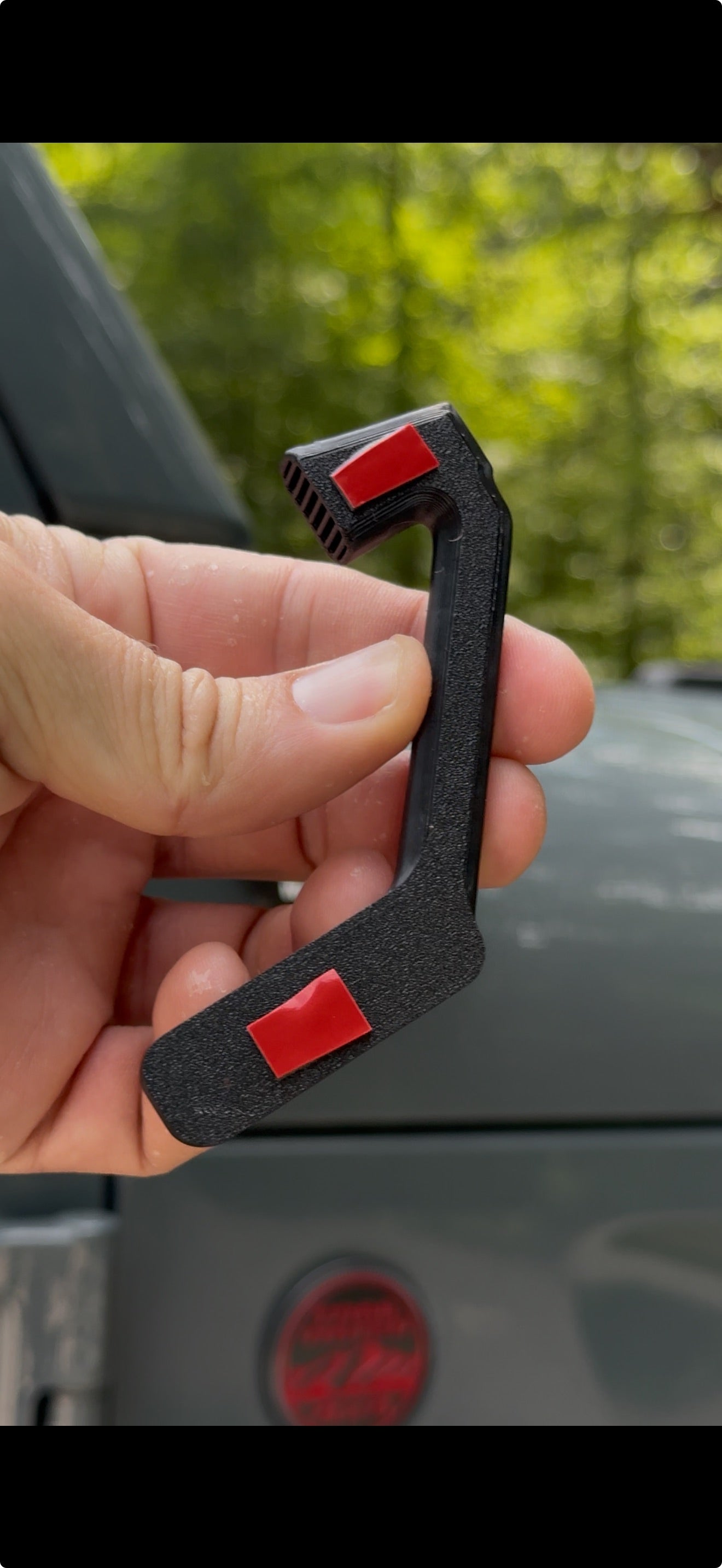 Hand holding a black carabiner with red buttons against a blurred outdoor background