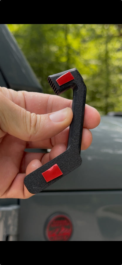 Hand holding a black carabiner with red buttons against a blurred outdoor background
